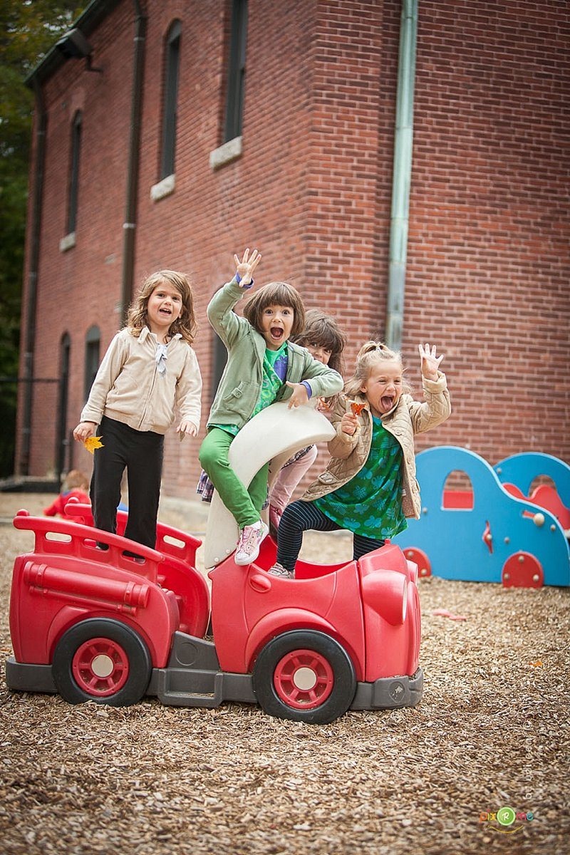 Children cheering on a red playground car